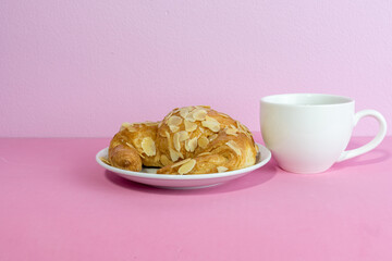 Obraz na płótnie Canvas Almond croissant and a cup of coffee on pink background.