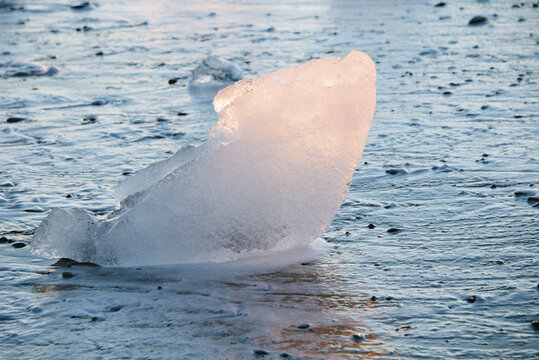 A large piece of translucent ice in the sea with waves in the background.