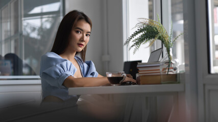 Young businesswoman working on her project while looking at the camera in office