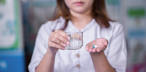 Close up cropped image millennial mixed race girl holding pill and glass of fresh water, taking medicine from head ache, stomach pain or , sedation meds, healthcare concept