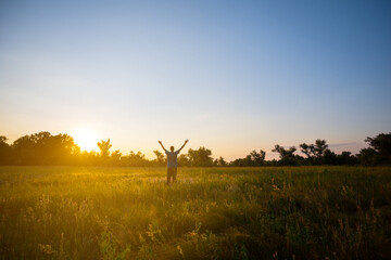 Fototapeta na wymiar happy man see off evening sun among a green summer prairie, human emotion concept background