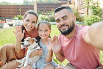 Father taking selfie shot of himself and his family waving hands at camera
