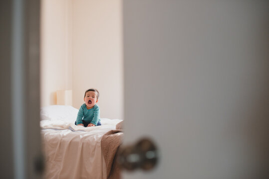 Little baby sitting up on bed, laughing and shouting
