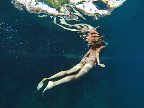 Skinny girl swimming underwater in clean blue sea