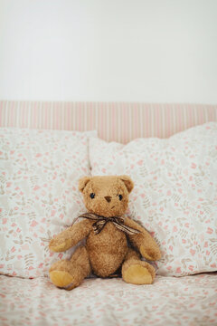 Teddy bear sitting amongst pillows on girl's bed