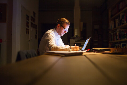 Young man working overtime in a dark office behind his laptop