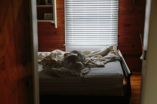 Messy bed sheets with bra in room of house after nap near window