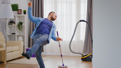 Excited young man dancing while cleaning his apartment.