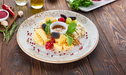 Cheese plate served with sauce, mint, nuts and fresh berries on a wooden background