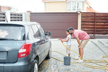 Modern father teaching his little son how to wash car, horizontal side view shot, copy space