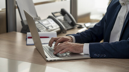 Male businessman typing on a laptop, working in the office, close-up, selective focus.