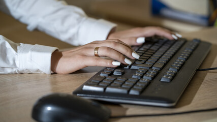 A female businessman in a white shirt typing on a keyboard, working in an office, close-up, selective focus.