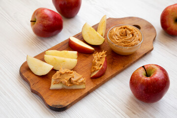 Raw Red Apples and Peanut Butter on a rustic wooden board on a white wooden surface, side view. Close-up.