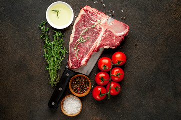 raw t-bone steak with ingredients on a meat knife on stone  background