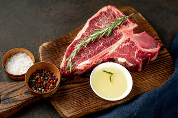 raw t-bone steak with ingredients on a wooden cutting board on a stone background