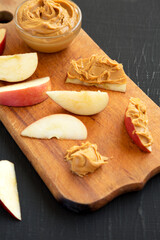 Raw Red Apples and Peanut Butter on a rustic wooden board on a black background, low angle view.