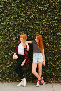 Two friends standing against a green plant wall