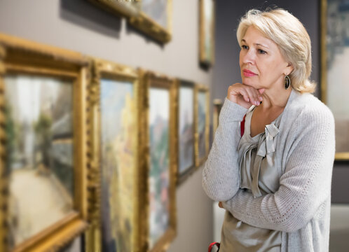 Portrait of positive mature woman near picture collection in the museum