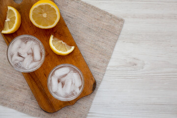 Fototapeta na wymiar Fresh Lemon Sparkling Water with Ice on a rustic wooden board on a white wooden background, top view. Overhead, from above. Copy space.