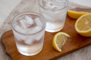 Fresh Lemon Sparkling Water with Ice on a rustic wooden board, side view. Close-up.