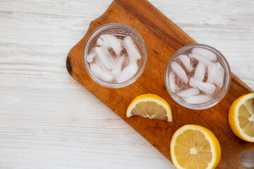 Fresh Lemon Sparkling Water with Ice on a rustic wooden board on a white wooden background, top view. Copy space.