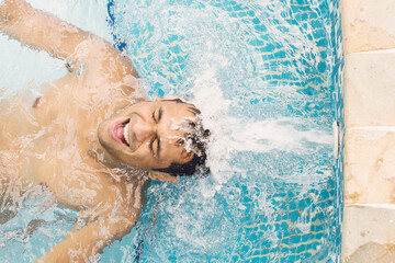Happy man being splashed by water jets in pool