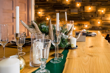 A decorated christmas dining table with wine glasses and christmas lights .Festive table setting among winter decorations and white candles. family dinner.New year candle ornament on wooden table