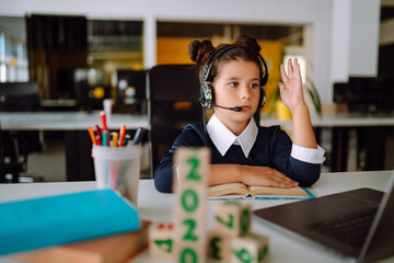 Fototapeta premium Online remote learning. Distance education. The girl raises her hand to answer the teacher's question. Covid-2019.