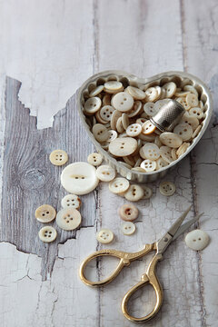 Heart shaped container with pearl buttons and scissors on wood