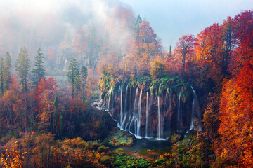 Incredible view on foggy waterfall in Plitvice lakes. Orange autumn forest on background. Plitvice...