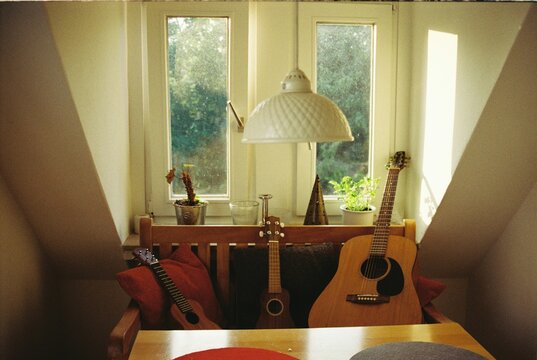 Two ukuleles and a guitar resting on a bench inside of a house