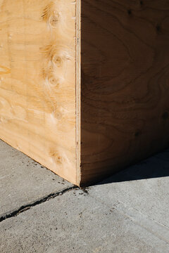 Corner of plywood wall, casting shadow on concrete sidewalk