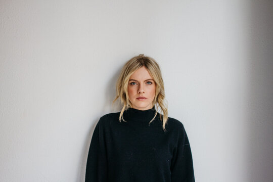 Young blonde female wearing dark sweater in front of white wall