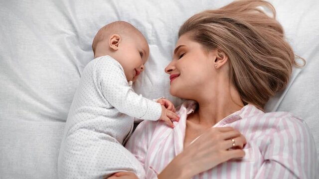 Happy mother and baby lying on bed together feeling love and tenderness. Medium shot on RED camera
