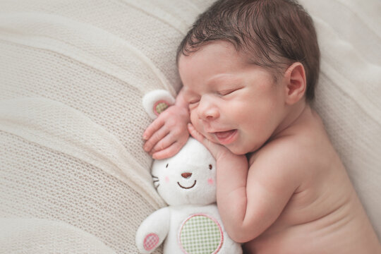 Smiling newborn baby sleeping with a white bunny toy.