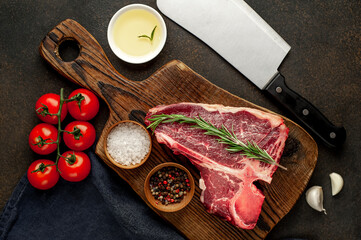 raw t-bone steak with ingredients on a wooden cutting board on a stone background