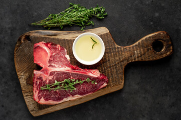 raw t-bone steak with ingredients on a wooden cutting board on a stone background