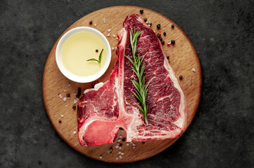 raw t-bone steak with ingredients on a wooden cutting board on a stone background