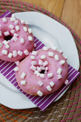 Pink glazed donuts with little marshmallow on a plate on wooden background