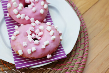 Pink glazed donuts with little marshmallow on a plate on wooden background