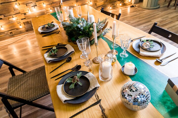 Stylish Christmas table setting, candle, mirror ball on big wooden table.Modern interior, new year decor ,Decorated living room.Celebration. Christmas Dinner. Holiday Decorations.Romantic dinner setup