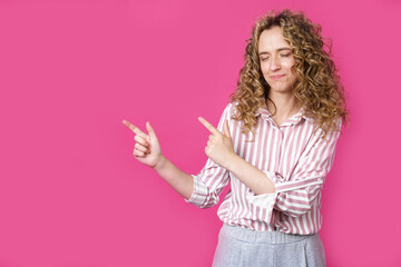 A cheerful woman points to a copy space, discusses an amazing ad, gives way or a direction, wears a striped shirt, has a pleasant smile, and feels optimistic