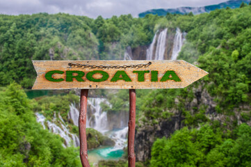 Fototapeta na wymiar Wooden arrow road sign with word Croatia against waterfall and forest background. Travel to Croatia concept.