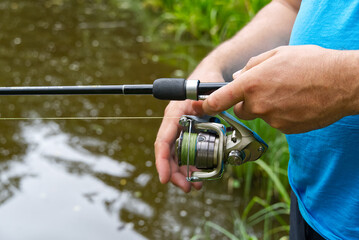 fisherman hand with spinning and reel on the summer lake, close-up.
