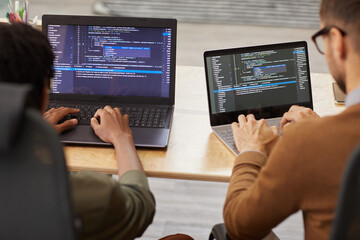 Rear view of two graphic designers sitting at the table and typing on their computers they...
