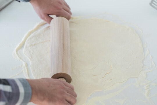 Man hands using roller pin on flat pizza dough base
