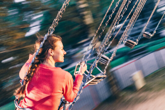 Young woman riding on a swing carousel in amusement park smiling