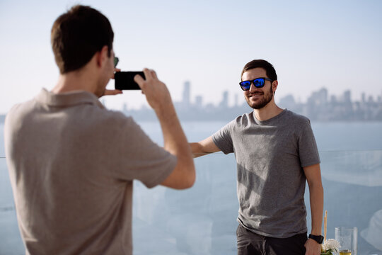Man taking picture of friend on a rooftop lounge bar with the city in the background