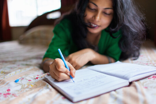Young woman writing on her diary while lying on bed