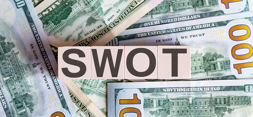 Fototapeta na wymiar Concept words SWOT on wooden blocks on a beautiful background from dollar bills.